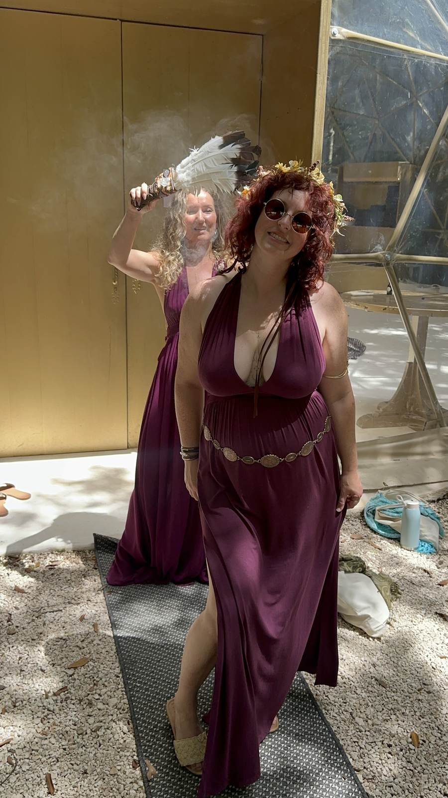 Two women in plum priestess gowns, one fanning copal smoke with a feather fan before the gold dome