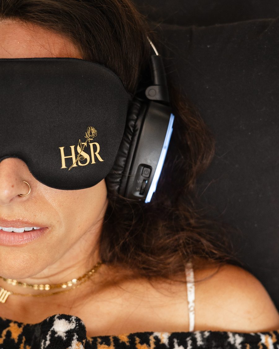A sister lying back in the gold embroidered eye mask and headphones, smiling as the ceremony begins