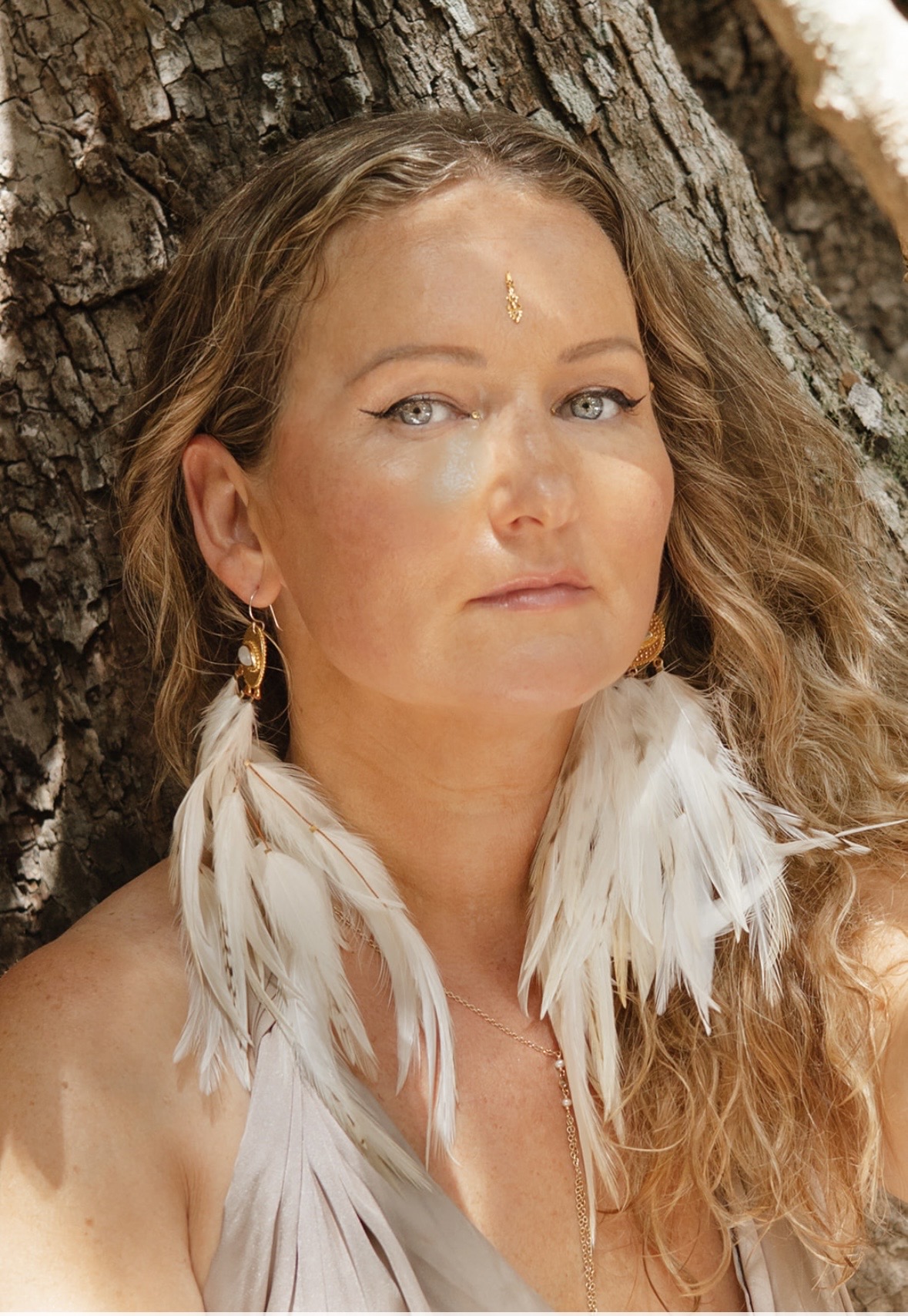 Anya Dillon at the roots of a jungle tree, feather earrings and a gold bindi