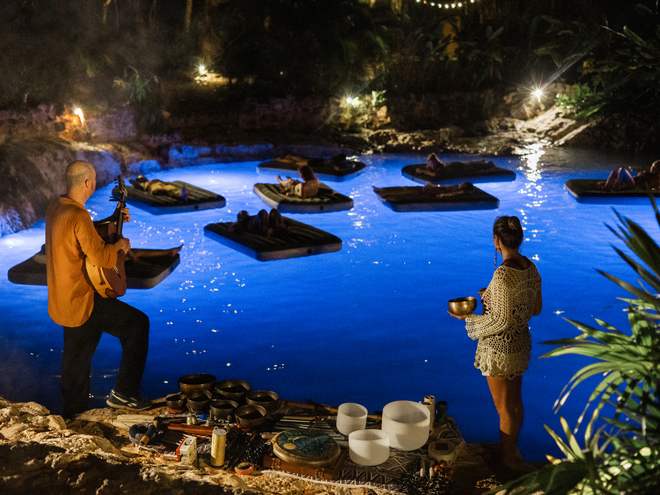 Sisters floating on the cenote at night while a musician and singing bowls carry the sound across the water