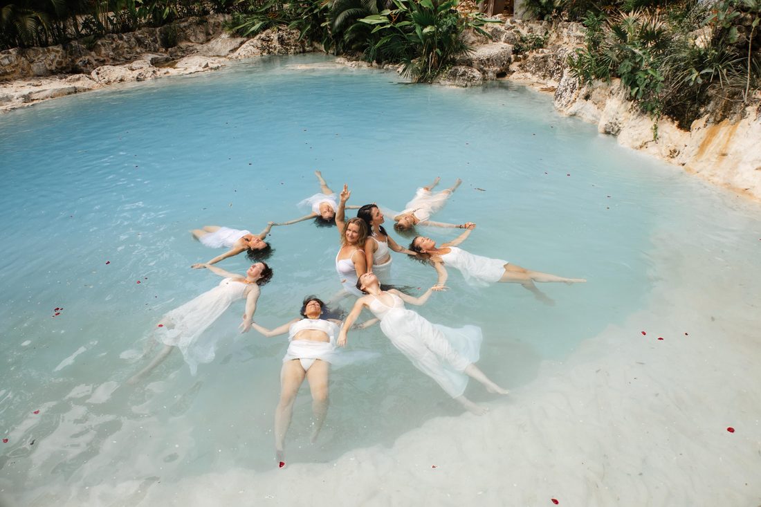 Sisters in white floating together in a star on the turquoise water, rose petals around them