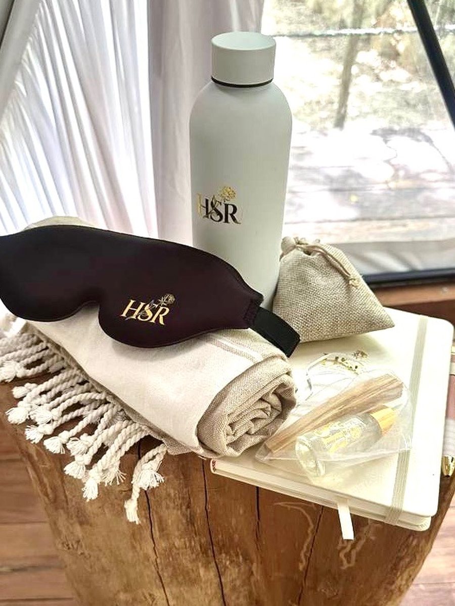 Her Sacred Rebirth welcome gifts laid out in the dome: gold monogrammed eye mask, water bottle, journal and pen, woven towel, and palo santo