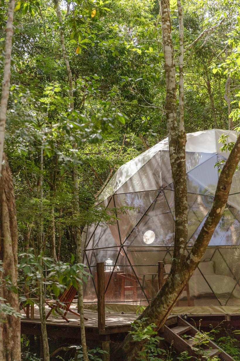 A private sleeping dome nestled among jungle trees at Amaite, wooden deck and white bed glowing through the glass