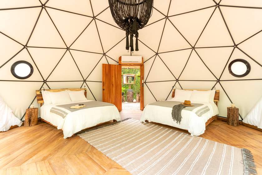 Shared dome interior with two queen beds, wooden floors, and a woven chandelier