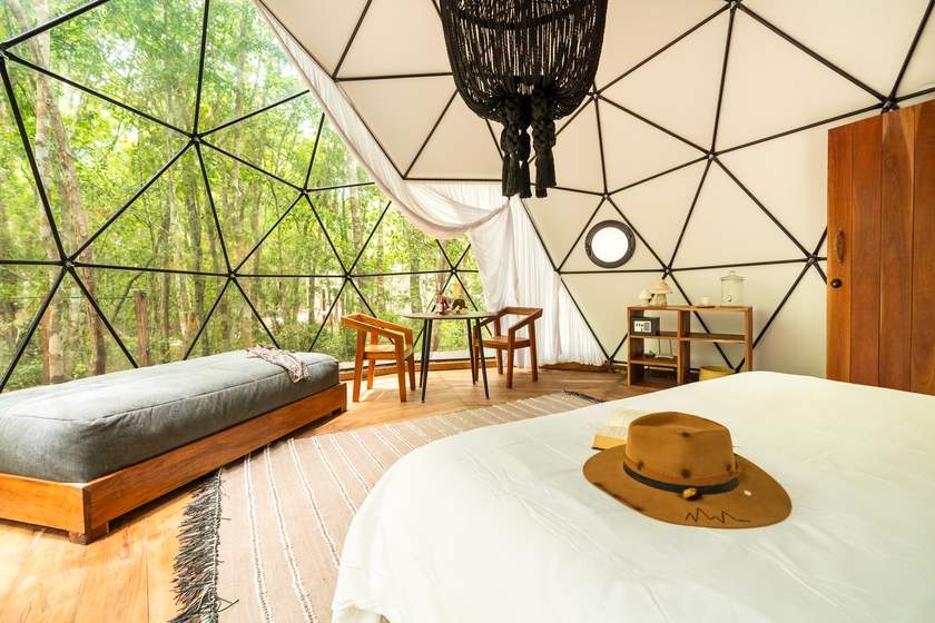 Solo dome interior with a queen bed and daybed looking out through glass walls into the jungle