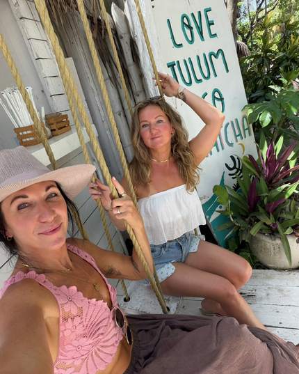 Anya and Bre laughing together on a swing at a Tulum beach cafe