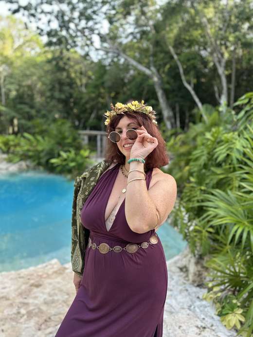 Melissa in a flower crown and plum gown beside the turquoise water