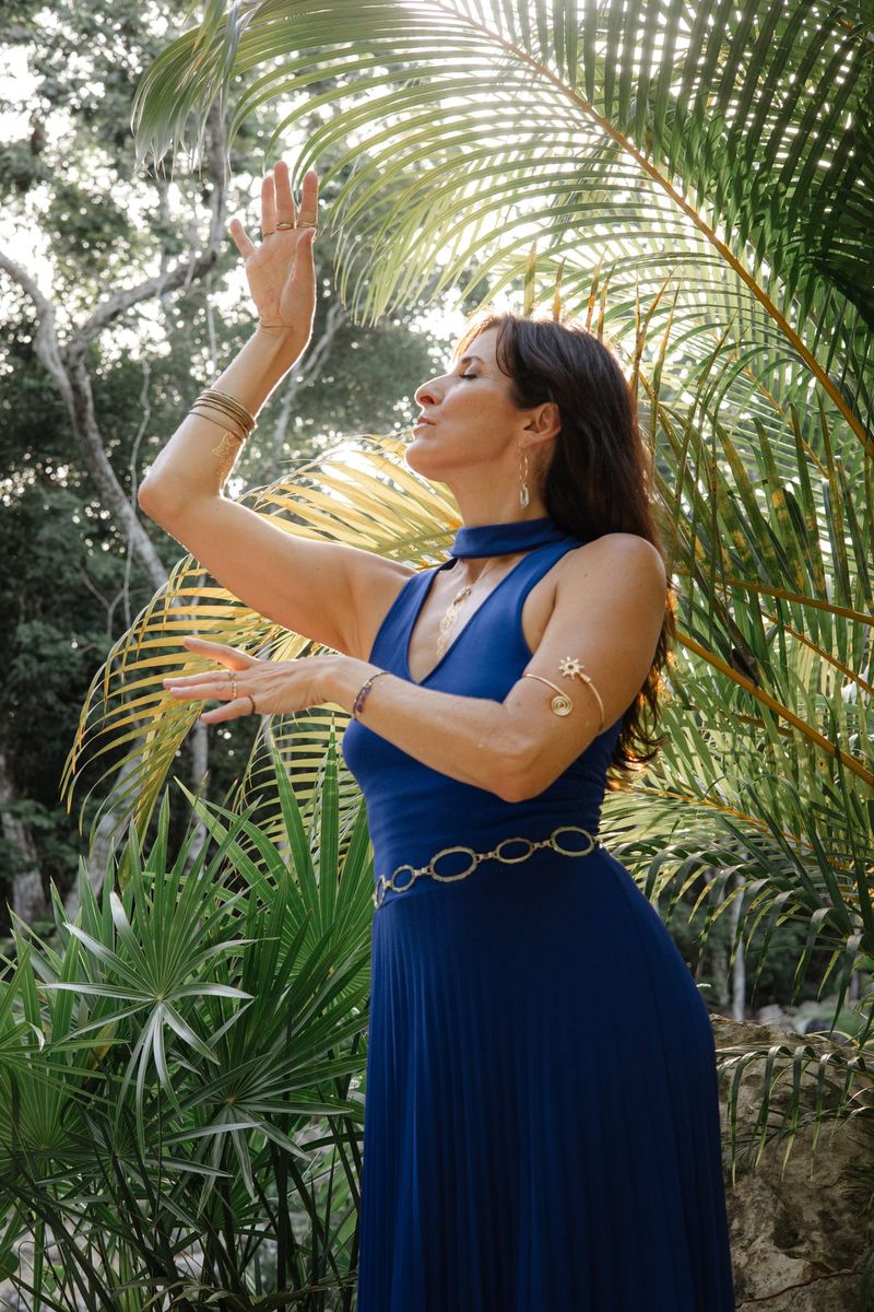 Brookelin in blue, arms lifted beneath a palm frond