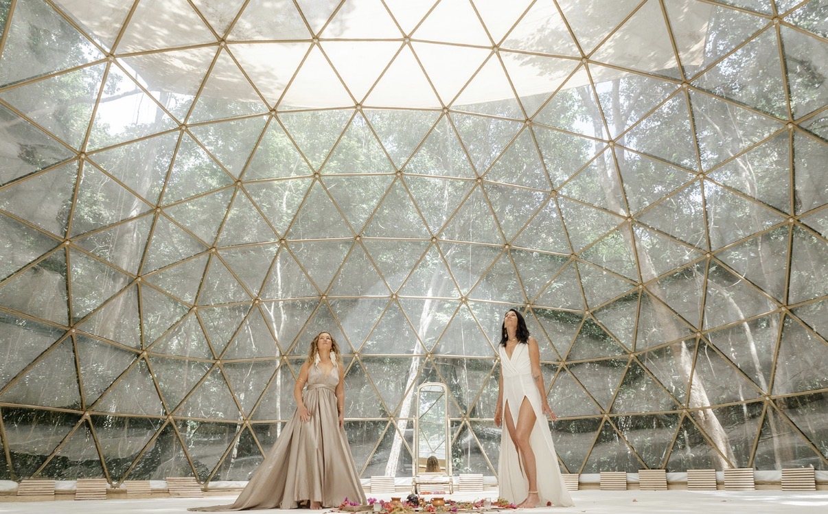 Anya and Bre standing inside the geodesic dome at Amaite, jungle visible through the glass